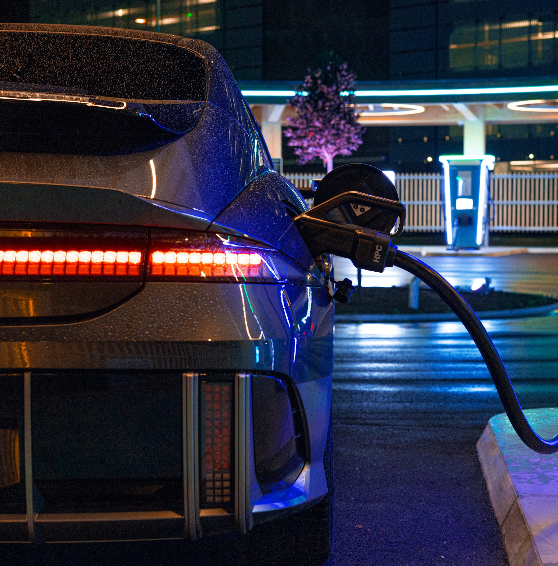 Electric vehicle charging at night, with light reflected in the wet pavement